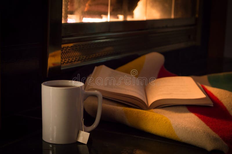 A good book and a cup of tea by a cozy fire. stock photo