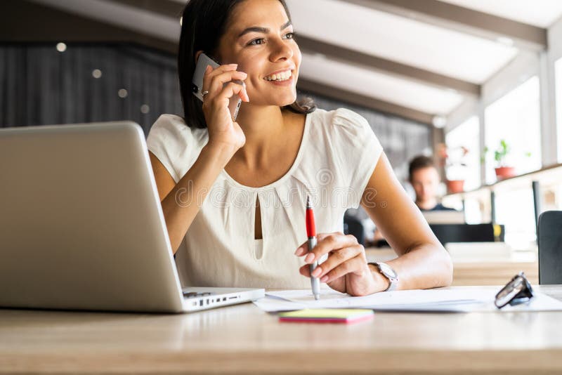 Good business talk. Cheerful young beautiful woman talking on mobile phone and using laptop with smile while sitting at