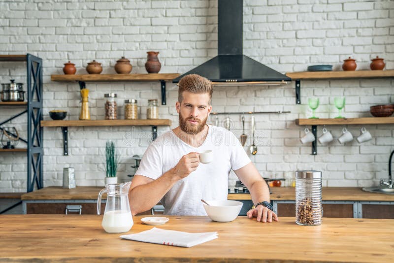 Good looking handsome bearded man is sitting in the kitchen drinking morning coffee with cereals and milk. reading morning press, royalty free stock photos Good looking handsome bearded man is sitting in the kitchen drinking morning coffee with cereals and milk. reading morning press, royalty free stock photos