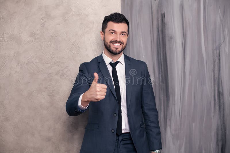 Good looking handsome happy businessman is standing in his office showing cool sigh and smiling. wearing suit and a tie royalty free stock image Good looking handsome happy businessman is standing in his office showing cool sigh and smiling. wearing suit and a tie royalty free stock image