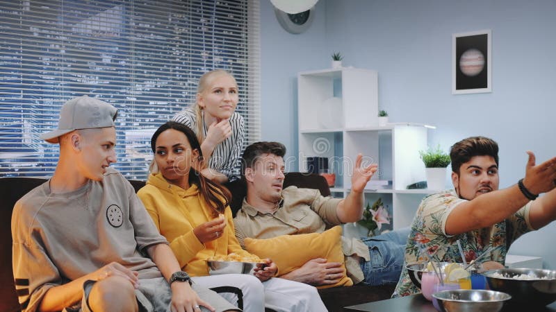 Good-looking men and women chatting at home and discussing action on TV stock photo Good-looking men and women chatting at home and discussing action on TV stock photo
