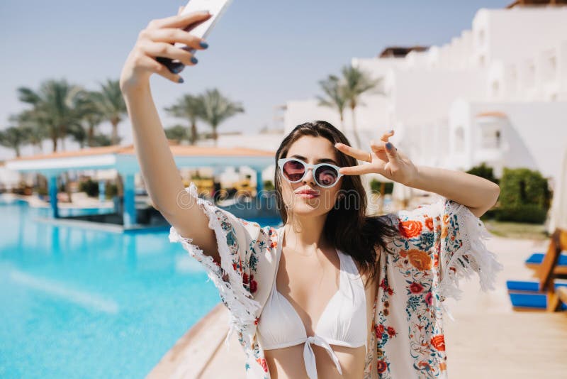 Good-looking stylish brunette girl resting on southern resort and making selfie before pool party with friends. Portrait