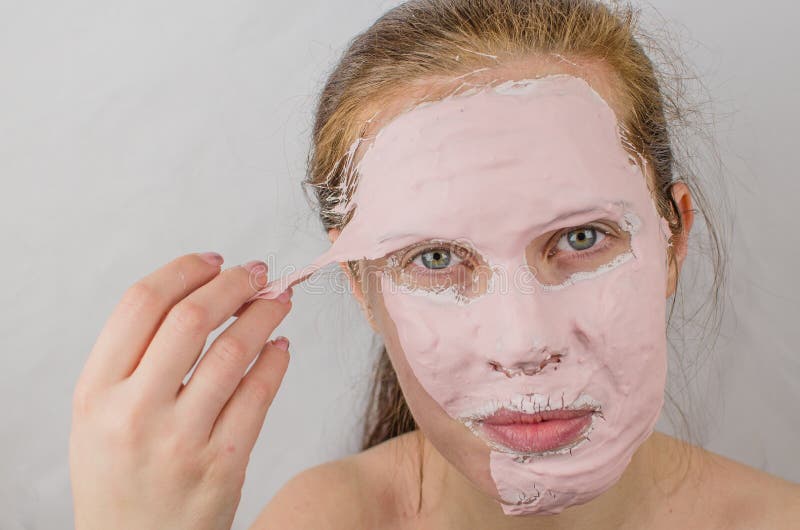 Good Looking Woman Having A Face Mask On Half Of Her Face Against Plain