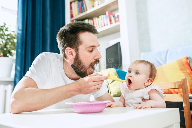 Good looking young man eating breakfast and feeding her baby girl at home