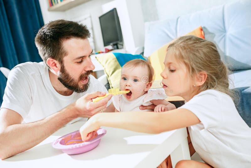 Good looking young man eating breakfast and feeding her baby girl at home