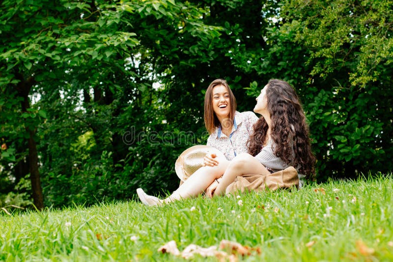 Cute girl friends having good moments sitting on the grass. Cute girl friends having good moments sitting on the grass