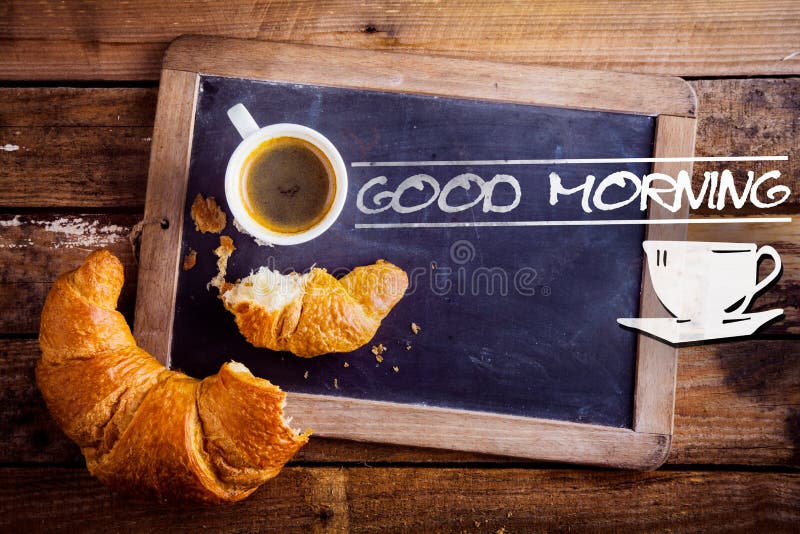 Good morning sign with a cup of fresh hot morning coffee and a broken croissant on an old school slate with a distressed wooden frame on a rustic table. Good morning sign with a cup of fresh hot morning coffee and a broken croissant on an old school slate with a distressed wooden frame on a rustic table