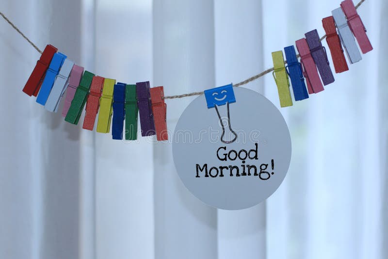 Good morning. Fresh good morning greeting concept with text notes on tag label paper hanging on rope with a smiling binder clip and colorful wooden clips decoration. New life, still life concept. Good morning. Fresh good morning greeting concept with text notes on tag label paper hanging on rope with a smiling binder clip and colorful wooden clips decoration. New life, still life concept