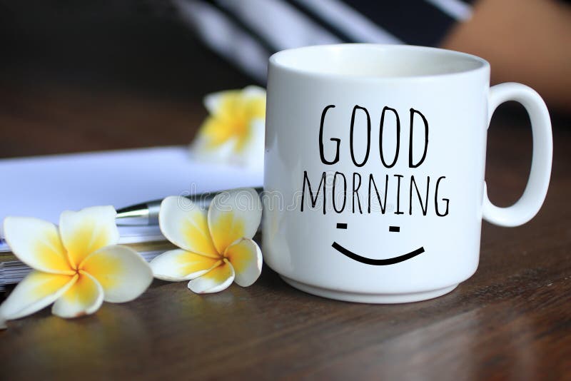 Morning coffee concept. Good morning text greeting on a cup of morning coffee with Bali frangipani flowers, paper work on desk  and an happy smile. Business plans, have a beautiful and productive day concept.