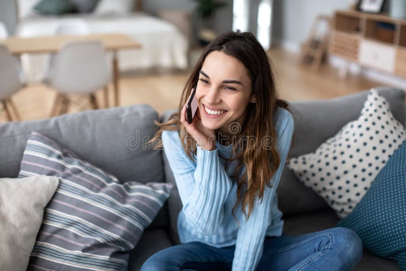 Attractive young woman talking on phone and smiling while sitting on a sofa at home