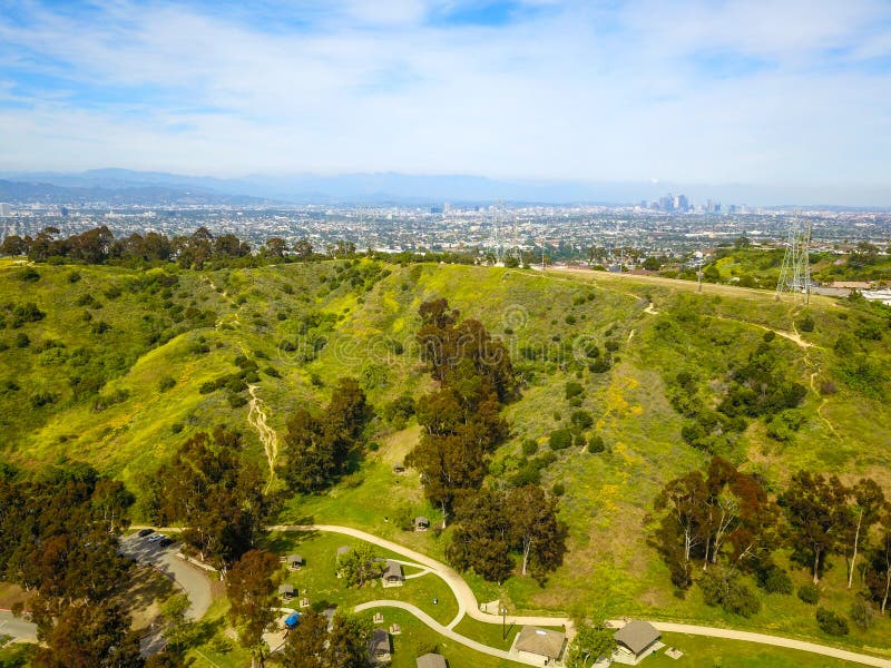 Gorgeous aerial shot of lush green hills in the city of Los Angeles around Kenneth Hahn Park with blue sky. In California