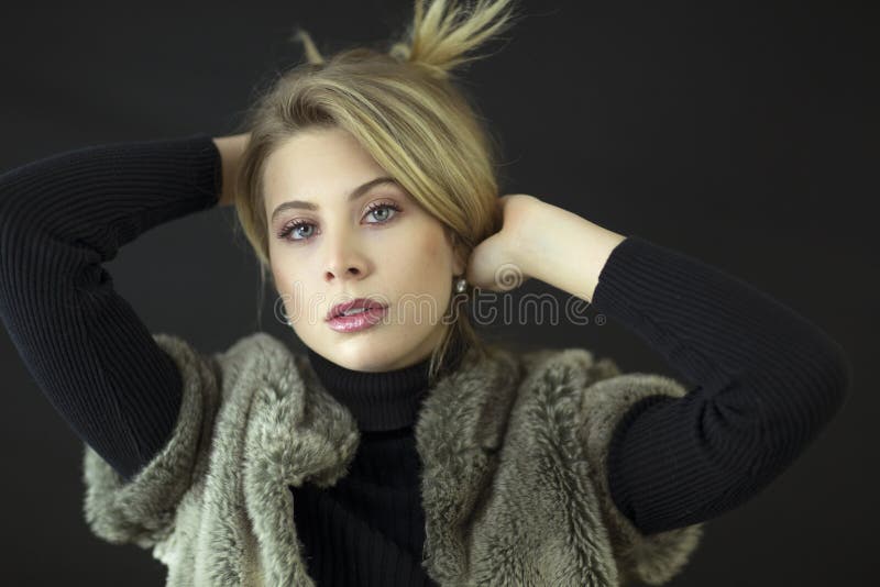 A gorgeous blond model with blue eyes and black turtleneck and fur vest in studio. royalty free stock photos A gorgeous blond model with blue eyes and black turtleneck and fur vest in studio. royalty free stock photos