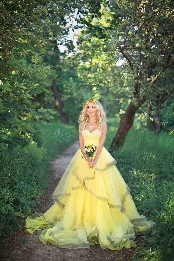 A gorgeous blonde girl in a yellow ball gown in a summer garden