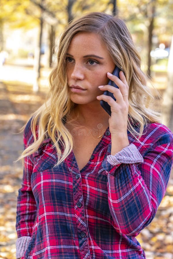A Lovely Blonde Talks On Her Mobile Device On An Autumn Day Outdoors At The Park Stock Image