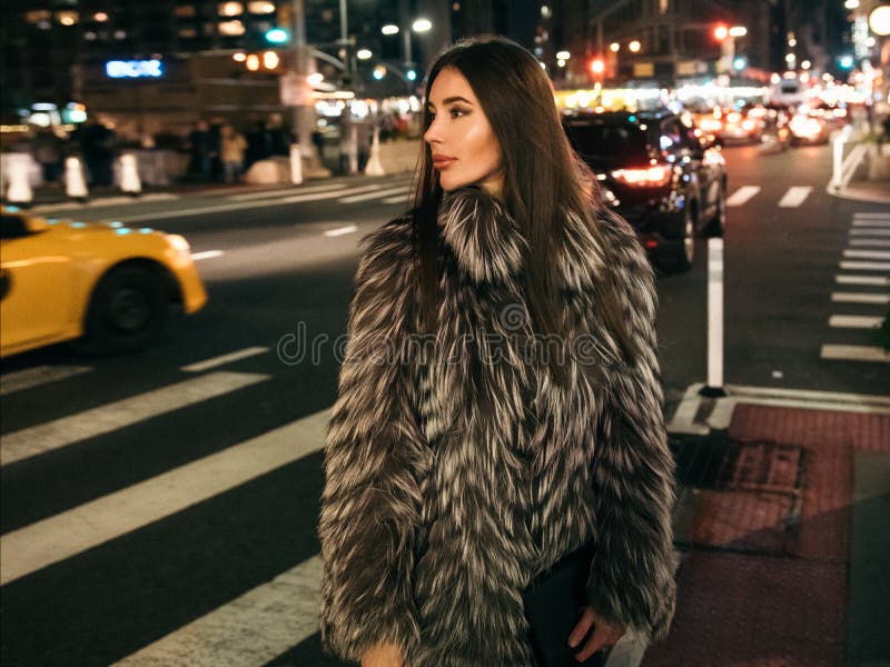 Gorgeous elegant woman walking on night city street wearing fake fur jacket and holding bag looking to the side. royalty free stock images Gorgeous elegant woman walking on night city street wearing fake fur jacket and holding bag looking to the side. royalty free stock images