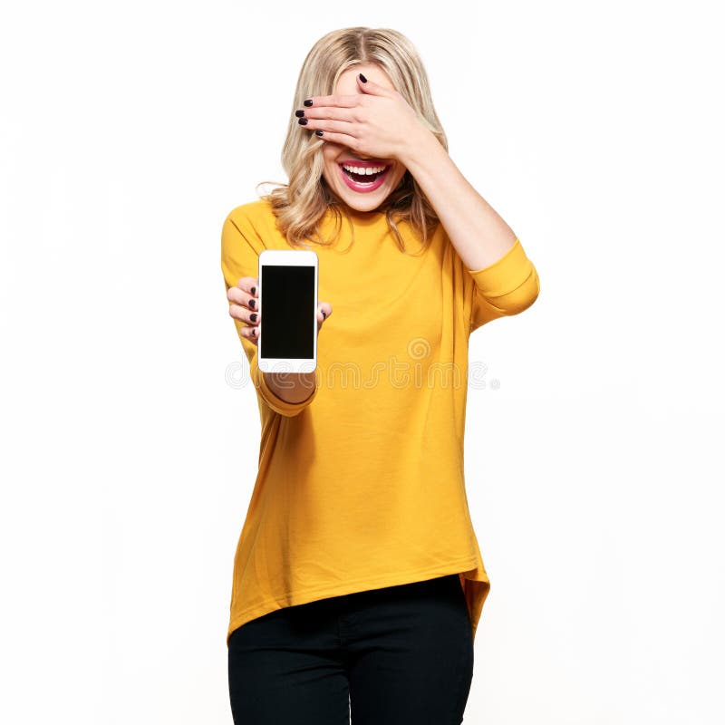 Gorgeous laughing woman showing blank screen mobile phone over white background, covering her eyes with hand. Very excited, cheering emotion.