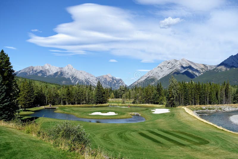 Gorgeous par 3 on a golf course surrounded by forest and big mountains in the background, on a beautiful sunny day in Kananaskis