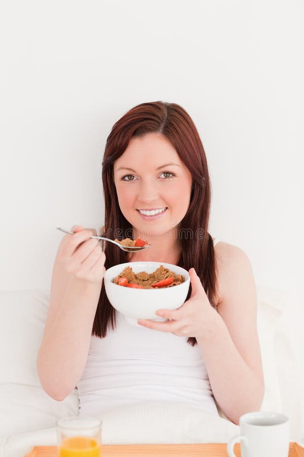 Gorgeous red-haired female having her breakfast while sitting on her bed