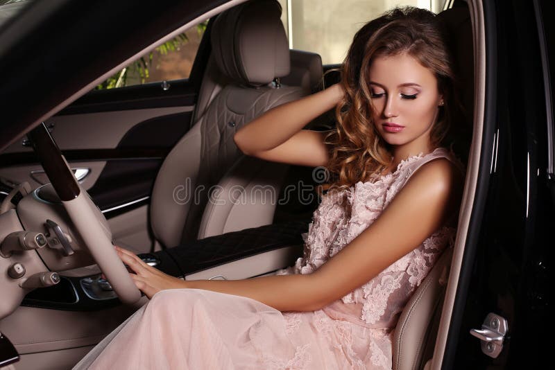 Gorgeous woman with dark hair wears luxurious dress,posing in black car