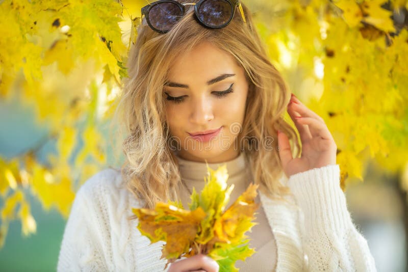 Gorgeous Young Woman Looks Down At Yellow Autumn Leaves In Her Hands