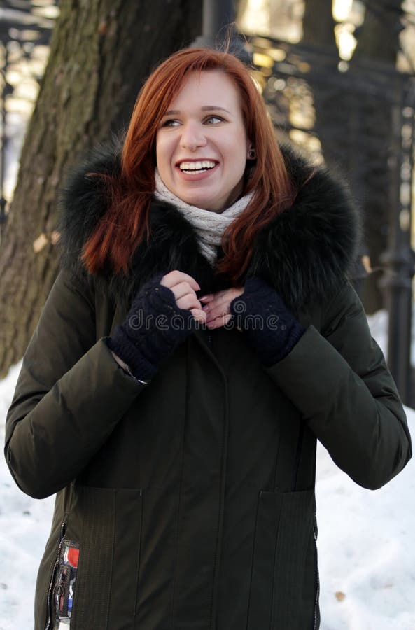 Young woman posing on the street in winter. Standing in clothes with a big fur hood. woman smiles. looking away royalty free stock photography Young woman posing on the street in winter. Standing in clothes with a big fur hood. woman smiles. looking away royalty free stock photography