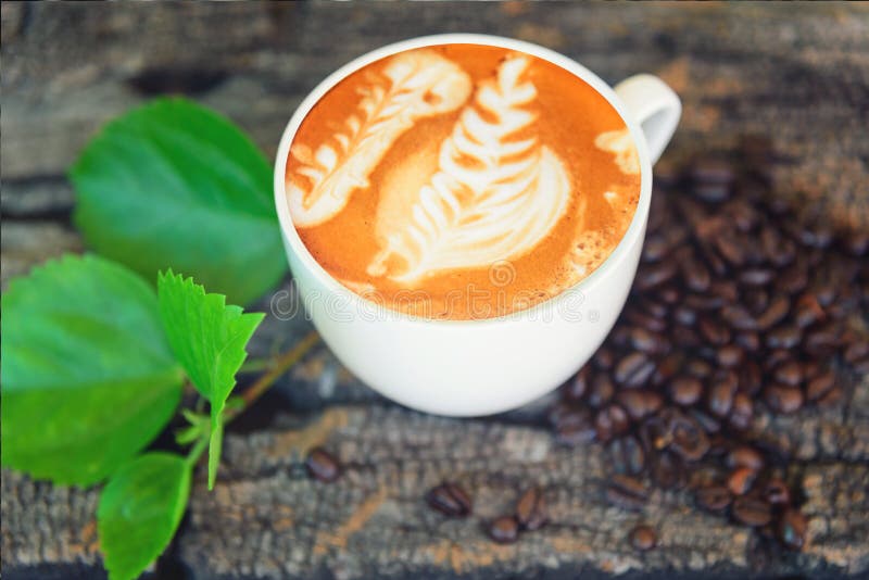 Gorący cappuccino z kawową fasolą i zieleń liściem na drewno stole fotografia royalty free Gorący cappuccino z kawową fasolą i zieleń liściem na drewno stole fotografia royalty free