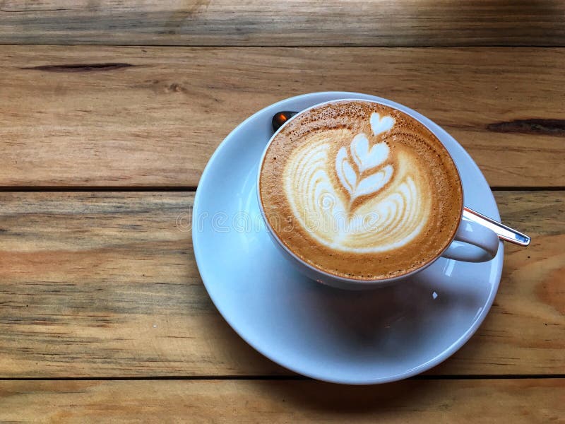 Gorąca cappuccino kawa w białym spodeczku z łyżką na drewnianym stołowym tle i filiżance Sztuka mleko piany rysunek zdjęcia stock