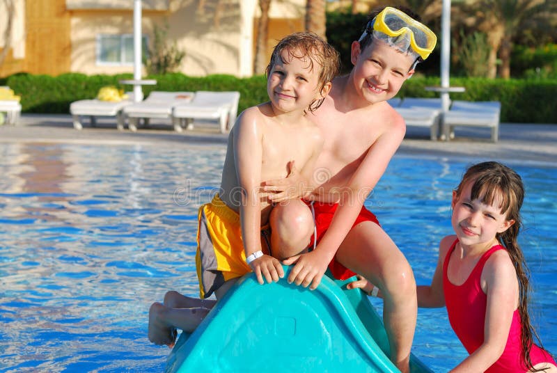 A view of three children playing on a slide in a swimming pool on a hot summer day. A view of three children playing on a slide in a swimming pool on a hot summer day.