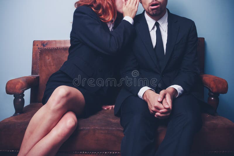 Young businesswoman is spreading gossip in the lobby to her male coworker who is very shocked. Young businesswoman is spreading gossip in the lobby to her male coworker who is very shocked