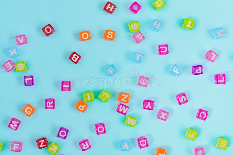 Gotas plásticas multicoloras del cubo con las letras dispersadas en fondo azul Textura del fondo del alfabeto fotografía de archivo Gotas plásticas multicoloras del cubo con las letras dispersadas en fondo azul Textura del fondo del alfabeto fotografía de archivo