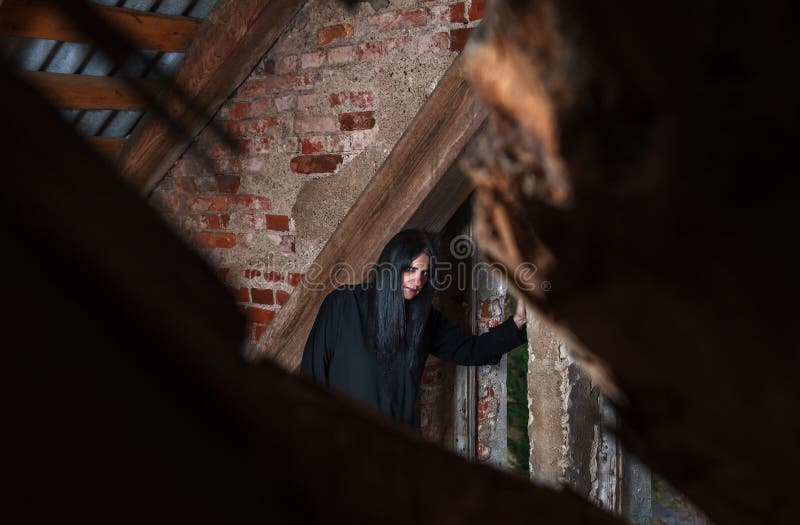 Gothic brunette woman standing near the window in attic