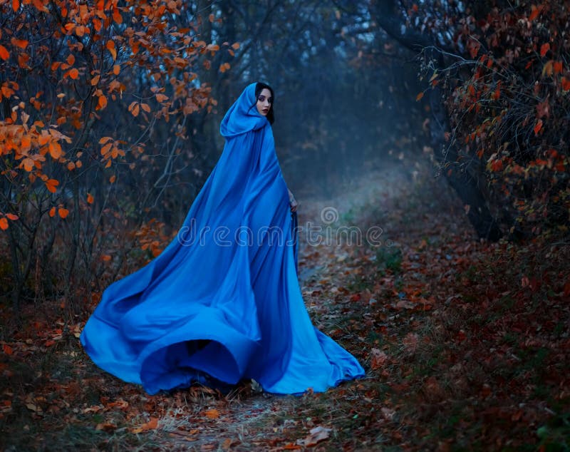 Gothic mysterious woman walks in fantasy autumn forest. long silk blue cloak flutters, waving fly in wind, fabric in