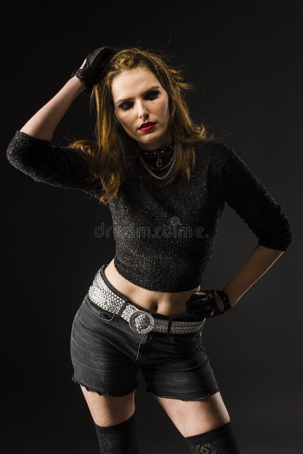 young woman standing in front of a dark background with hotpants and stockings stockings wearing leather gloves and runs his hand through the hair. young woman standing in front of a dark background with hotpants and stockings stockings wearing leather gloves and runs his hand through the hair