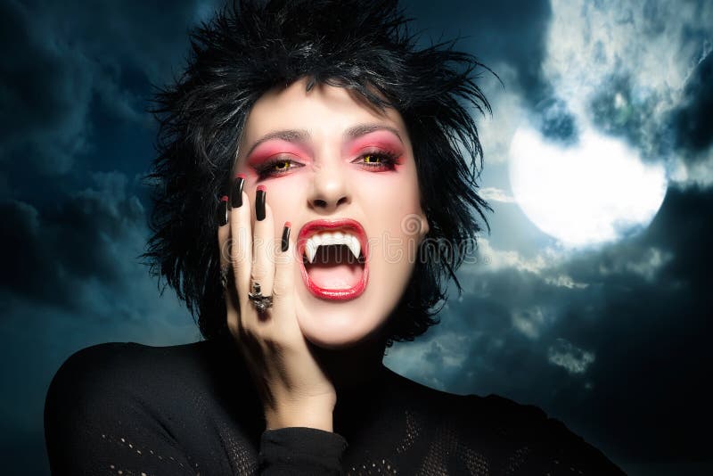 Female werewolf. Beautiful young woman screaming with fangs, wolf lenses and decorated nails. Halloween concept. Female werewolf. Beautiful young woman screaming with fangs, wolf lenses and decorated nails. Halloween concept