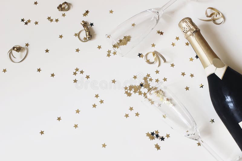 Gott nytt års sammansättning Champagnglas och vinflaska med gyllene konfektstjärnor på vitt bord arkivbild