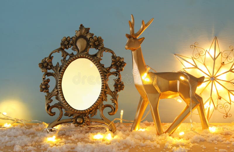 Gouden glanzend rendier en leeg fotokader op sneeuw houten lijst met de lichten van de Kerstmisslinger Voor fotografie en plakboe royalty-vrije stock foto's Gouden glanzend rendier en leeg fotokader op sneeuw houten lijst met de lichten van de Kerstmisslinger Voor fotografie en plakboe royalty-vrije stock foto's