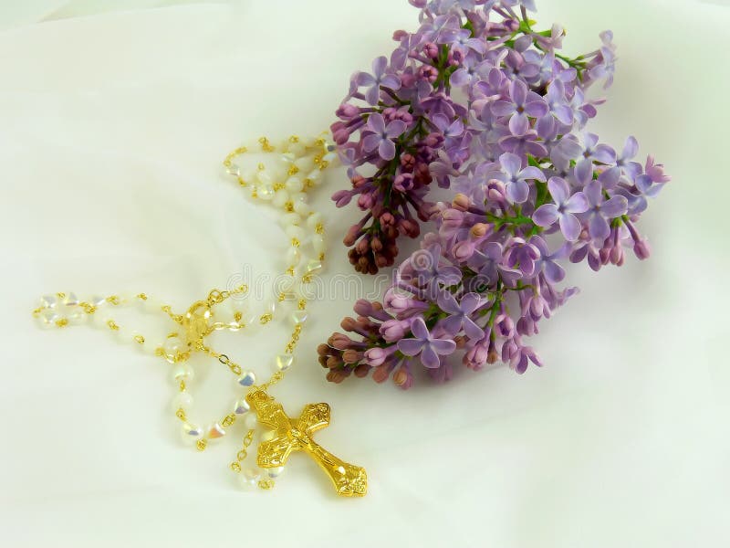 Gold Christian Catholic cross lying on romantic white veil surrounded with beautiful flower lilac, romantic gold religious jewelry with flower. Gold Christian Catholic cross lying on romantic white veil surrounded with beautiful flower lilac, romantic gold religious jewelry with flower