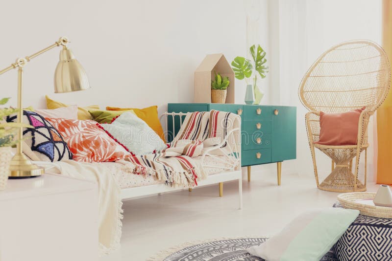 Gouden lamp op nightstand in de slaapkamer van het bohomeisje met kleurrijk beddegoed op bed, groene houten kabinet en pauwstoel royalty-vrije stock afbeelding Gouden lamp op nightstand in de slaapkamer van het bohomeisje met kleurrijk beddegoed op bed, groene houten kabinet en pauwstoel royalty-vrije stock afbeelding