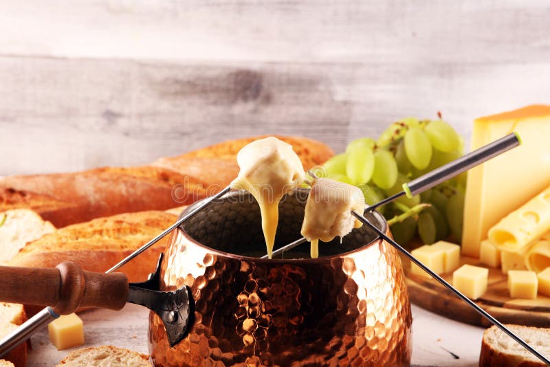 Gourmet Swiss fondue dinner on a winter evening with assorted cheeses on a board alongside a heated pot of cheese fondue with two