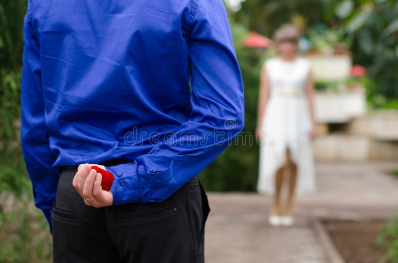 Governi nascondere la fede nuziale dietro il suo parte posteriore ed andare offrirlo ad una sposa fotografie stock libere da diritti Governi nascondere la fede nuziale dietro il suo parte posteriore ed andare offrirlo ad una sposa fotografie stock libere da diritti