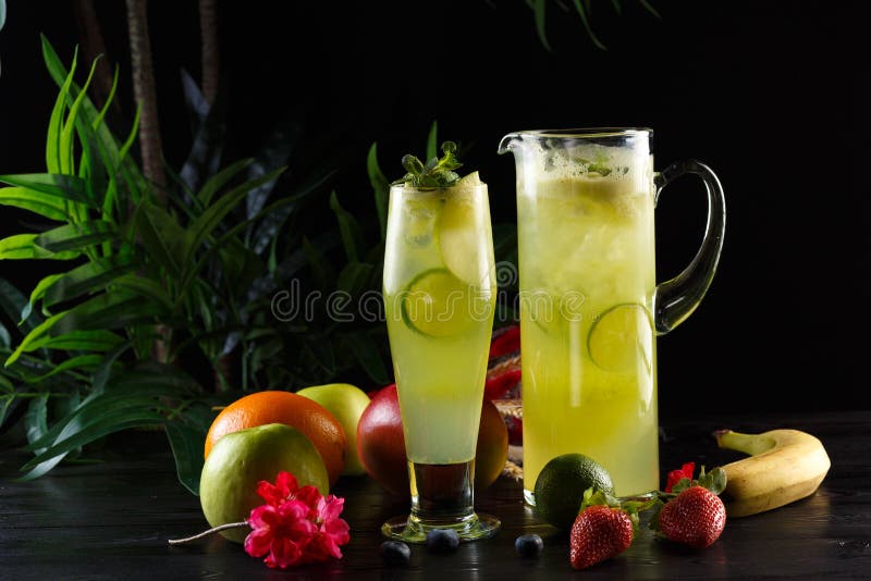 Gr?n ?pplelemonad med limefrukt i en tillbringare och ett exponeringsglas och frukter p? en m?rk bakgrund arkivfoton Gr?n ?pplelemonad med limefrukt i en tillbringare och ett exponeringsglas och frukter p? en m?rk bakgrund arkivfoton