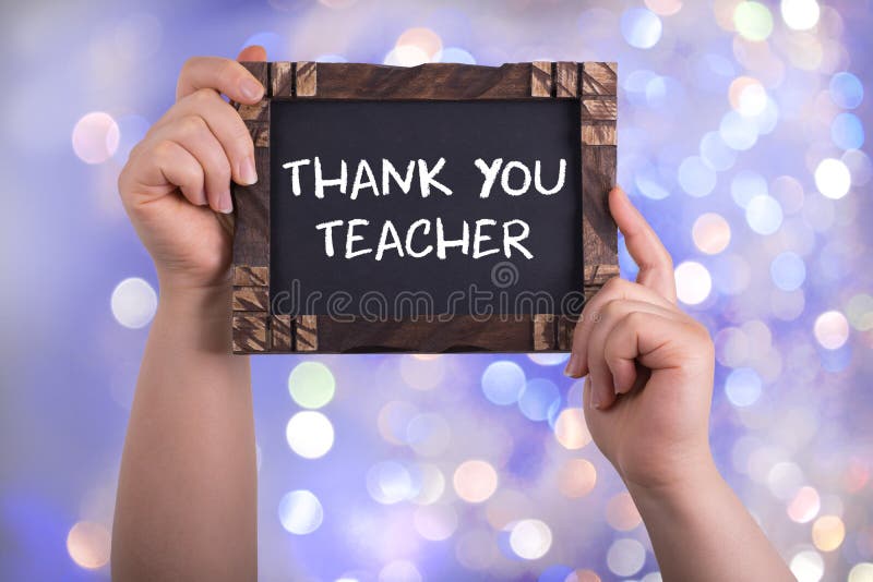 A woman holding chalkboard with words thank you teacher on bokeh light background. A woman holding chalkboard with words thank you teacher on bokeh light background.