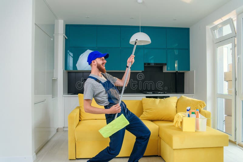 Graciosa foto de un trabajador de limpieza con ropa especial jugando con un trapo como guitarra en la cocina
