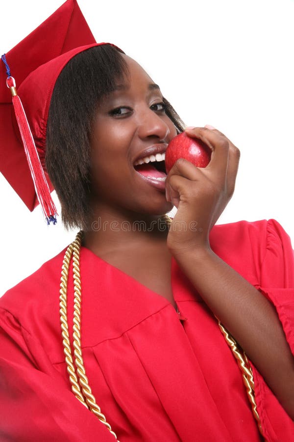 Portrait of happy black graduate with red gown and hat eating apple; isolated on white background. Portrait of happy black graduate with red gown and hat eating apple; isolated on white background.