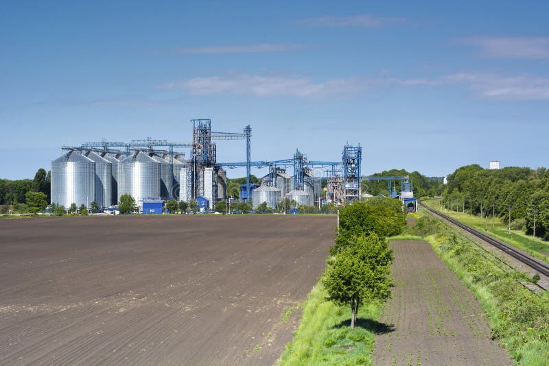Grain metallic silos of elevator and seed plant with railroad for shipment in the field of spring fields stock image Grain metallic silos of elevator and seed plant with railroad for shipment in the field of spring fields stock image