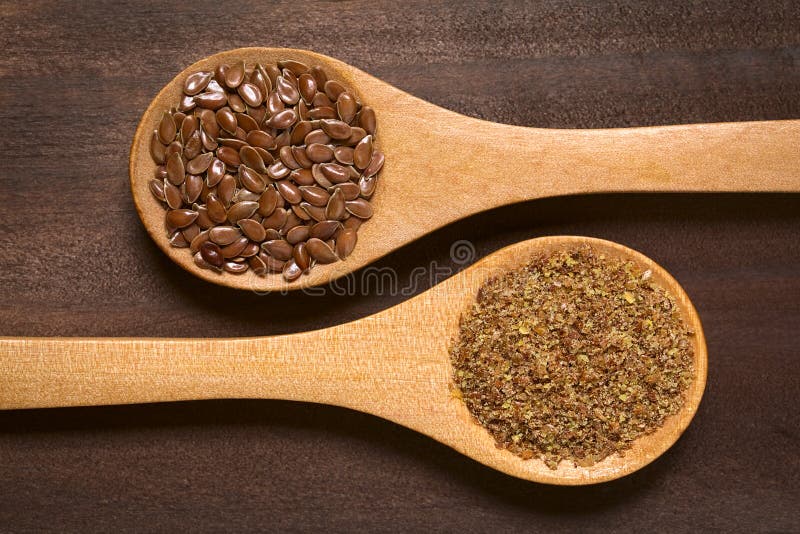 Whole and ground brown flax seeds or linseeds on wooden spoons, photographed on dark wood with natural light. Whole and ground brown flax seeds or linseeds on wooden spoons, photographed on dark wood with natural light