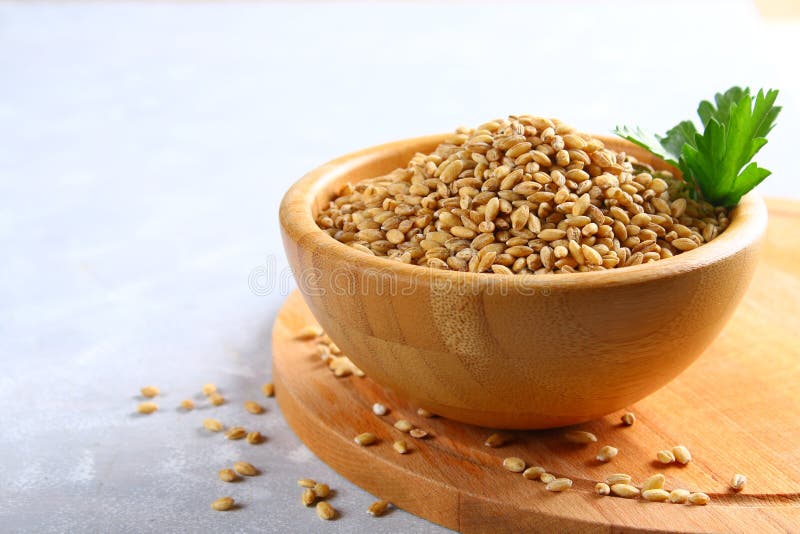 Grains of Pearl Barley in a Wooden Bowl on a Wooden Table. Stock Photo