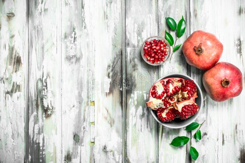 Grains and pieces of pomegranate in a bowl and whole pomegranates with leaves