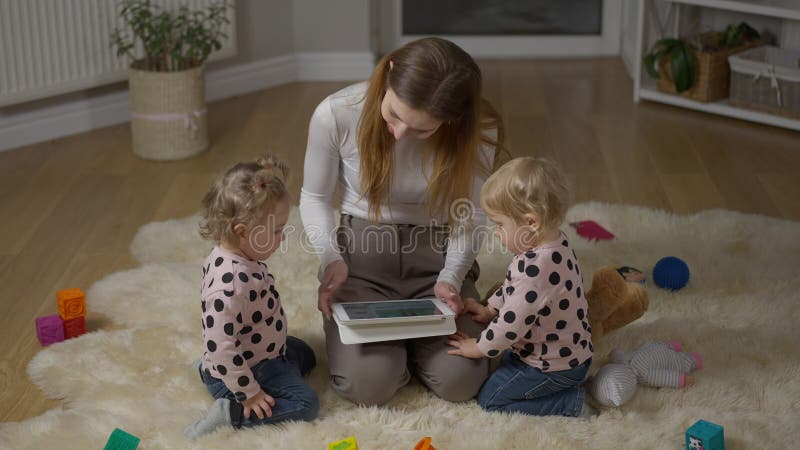Gran foto di donna millenaria felice e di due gemelle sedute sul pavimento in soggiorno con una tavoletta. sorridente rilassato stock footage