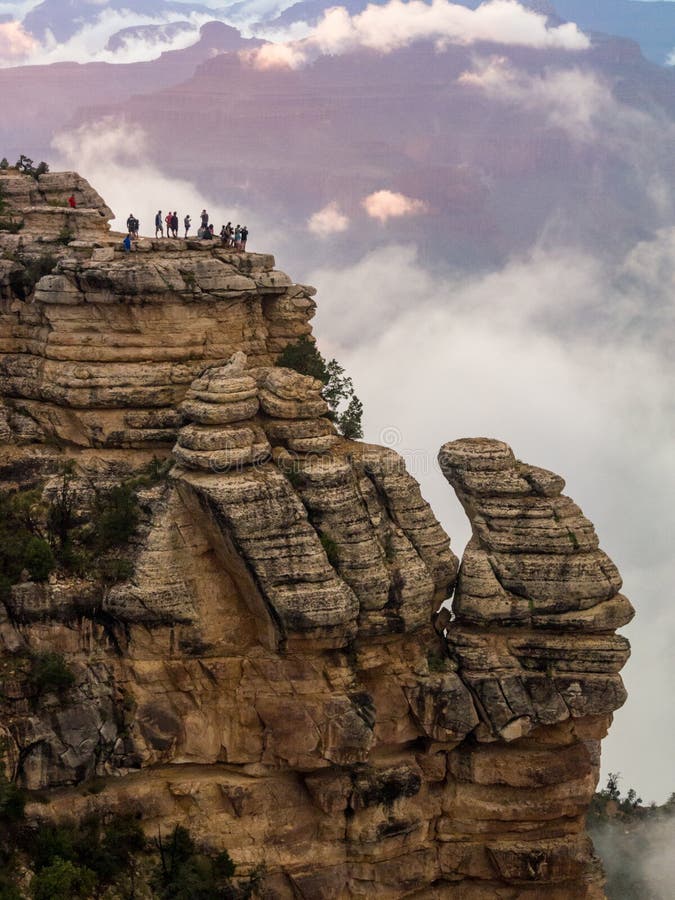 A prominent spire of rock along the edge of the Grand Canton, tourists on the cliff overlooking a cloudy canyon. A prominent spire of rock along the edge of the Grand Canton, tourists on the cliff overlooking a cloudy canyon.